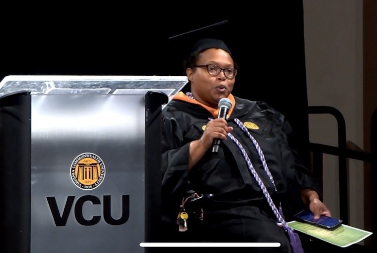 Woman in wheelchair speaking at ceremony in graduation cap and gown