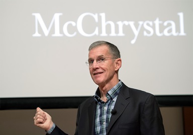 General Stanley McChrystal stands on a stage speaking. A sign behind him says his name. 