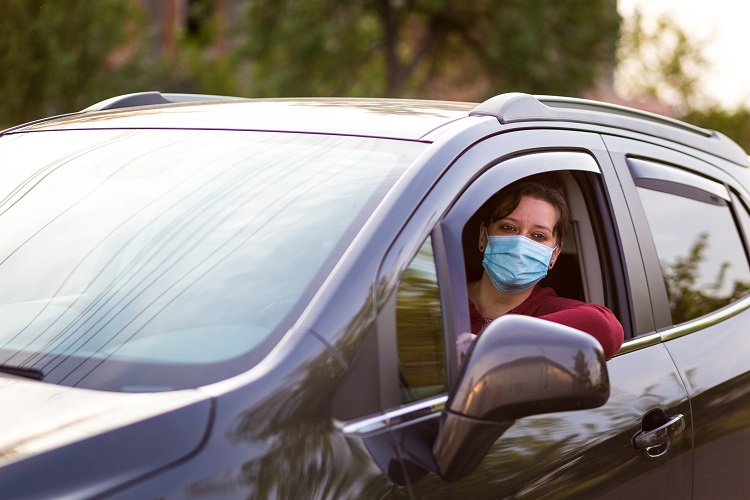 Masked woman sitting in the driver's seat of a car with the window down