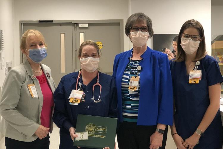 Daisy Award winner, Tiffany Foley, holding award and standing with CMH nursing team members