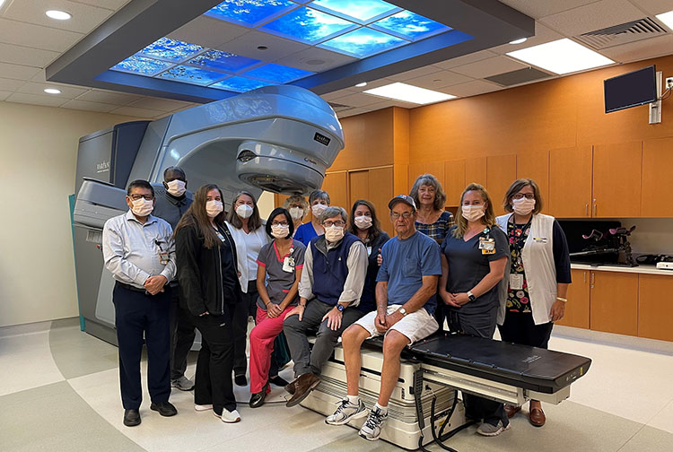 A husband and wife stand with radiation equipment and their care team.