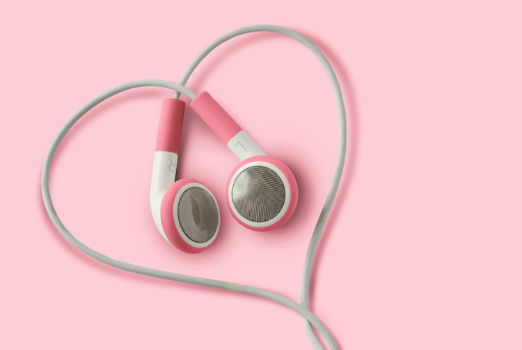 Headphones wrapped in the shaped of a heart with a pink background.