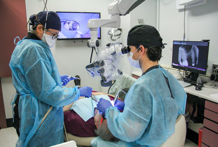 Two dentists working with a patient. They are examining his teeth.