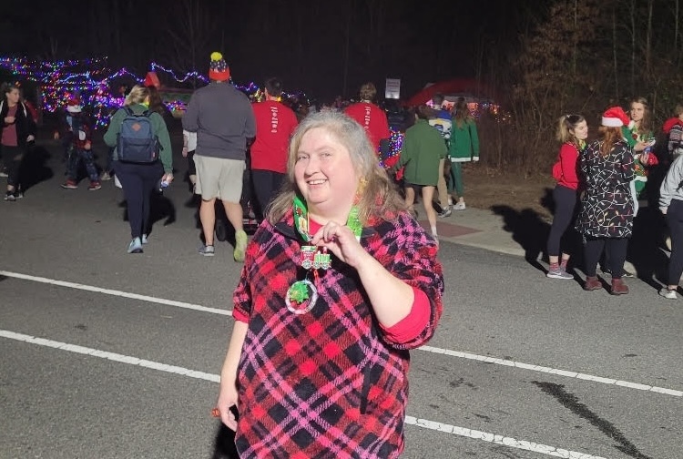 Woman dressed in festive holiday colors holds up her medal after a local fun run.