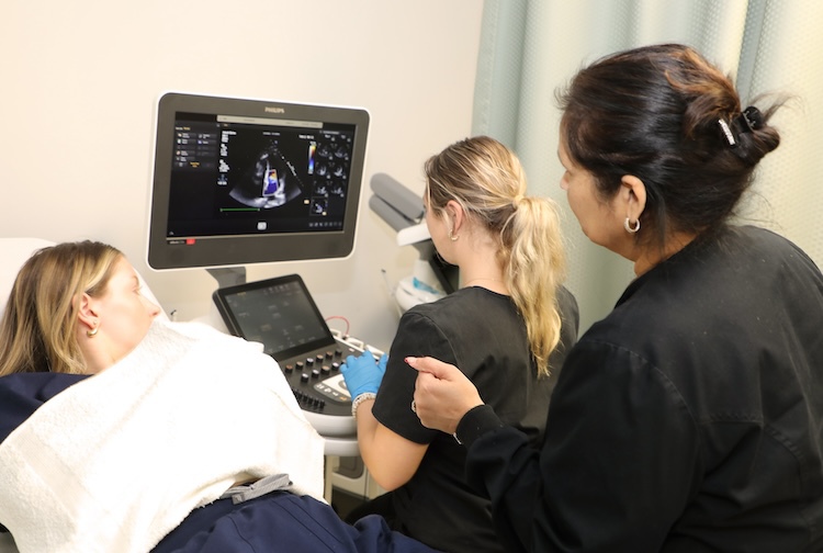 A professor and students look at the images of a student’s heart on a sonography machine.