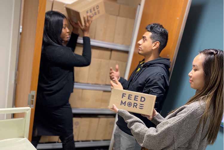Student volunteers retrieve boxes of food from a supply closet.