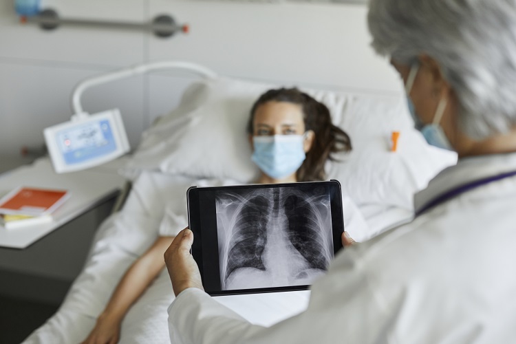 Female patient laying in bed next to doctor looking at chest x-ray