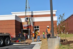 A linear accelerator is delivered to a brick building on a crane.