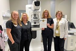 Health care workers pose with a mammography machine and certificate. 