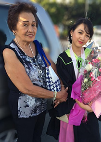 An older woman from the Philippines poses with a younger women from the Philippines holding a bouquet of flowers.