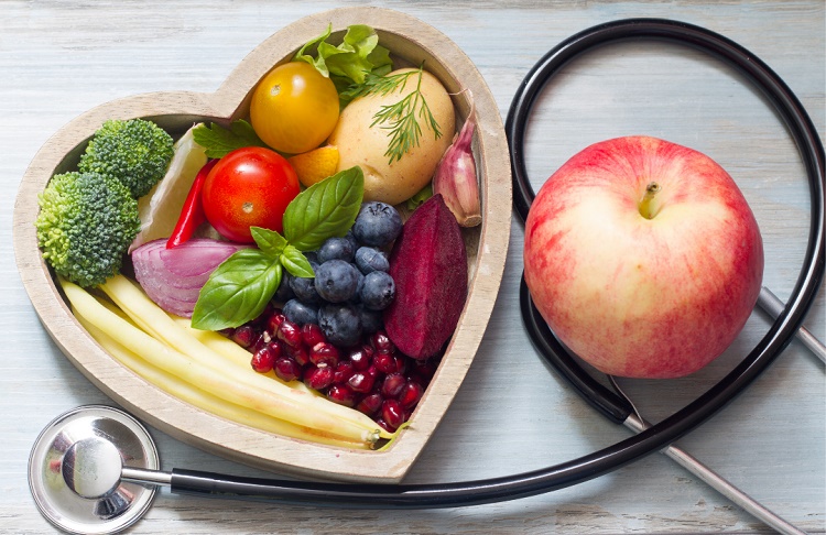 Fruits and vegetables in a heart-shaped bowl next to an apple and a stethoscope
