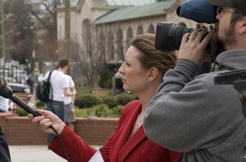 Journalist on the street with a microphone, standing next to a camera person.