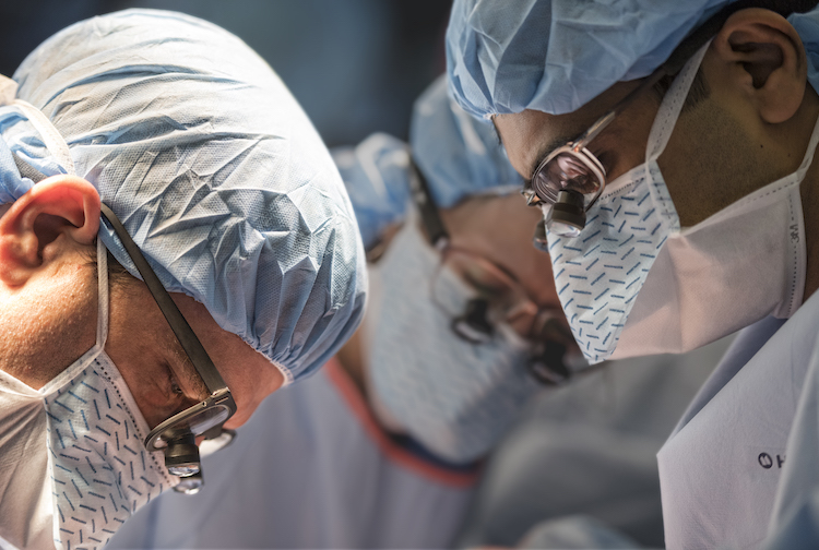 Close-up image of three doctors and nurses with their heads looking down as they perform surgery