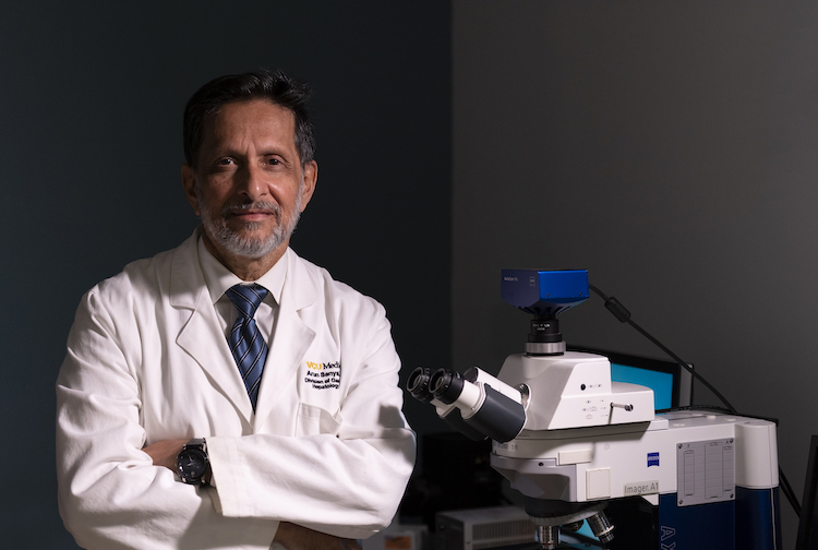 Dr. Sanyal stands with his arms crossed with a microscope