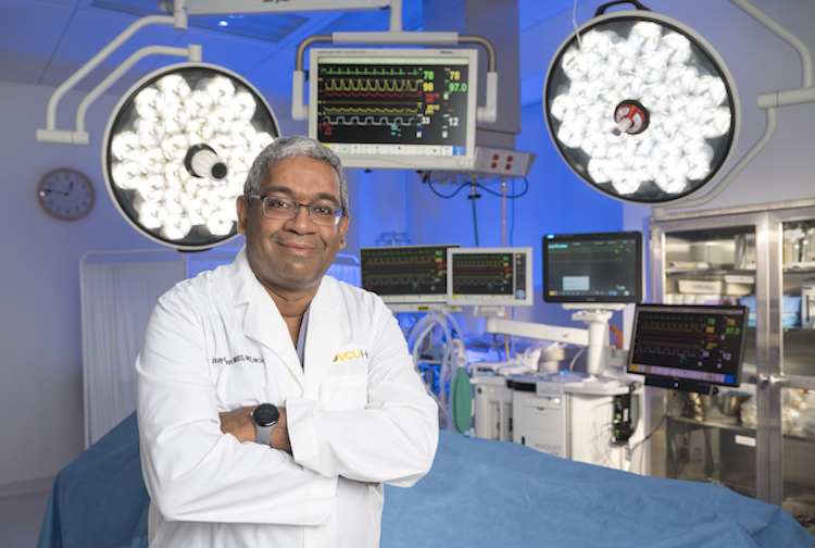 Dr. Kumaran stands in a white lab coat in front of an operating table.