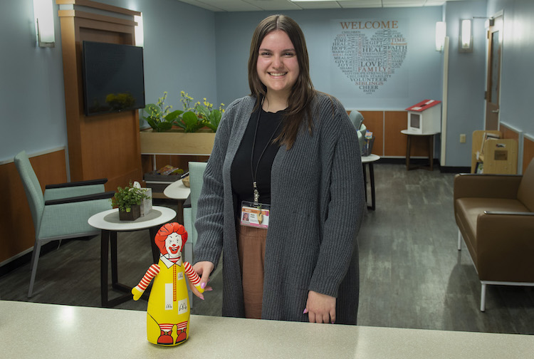 Young woman with brown hair smiles for the camera with a doll of Ronald McDonald, a clown with red hair and a yellow outfit.