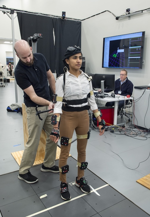 Male student calibrates sensor points on a female student. The female student is wearing several belts around her body with the sensor points. 