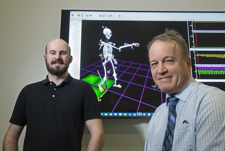Peter Pidcoe and graduate student Zach Moore stand near a monitor showing the skeletal representation of a participant wearing the motion-capture suit.