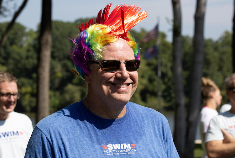 Man with sunglasses wears a rainbow wig styled as a mohawk.