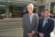 Images Two men in suits standing in front of the VCU Health sign