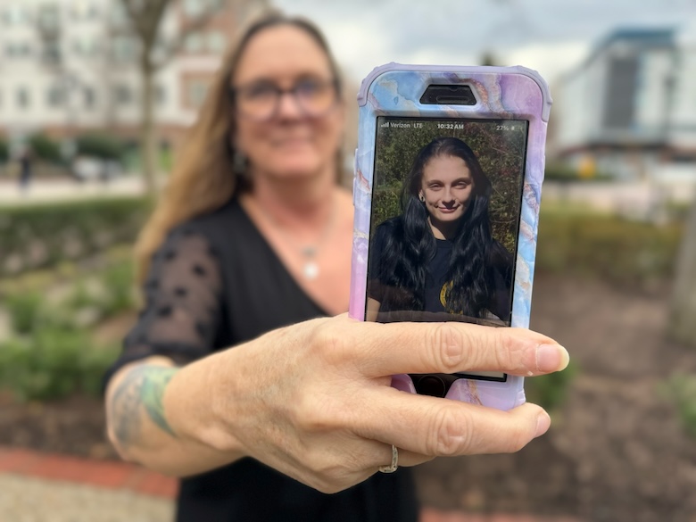 woman stands in park holding up a phone with a photo of a girl