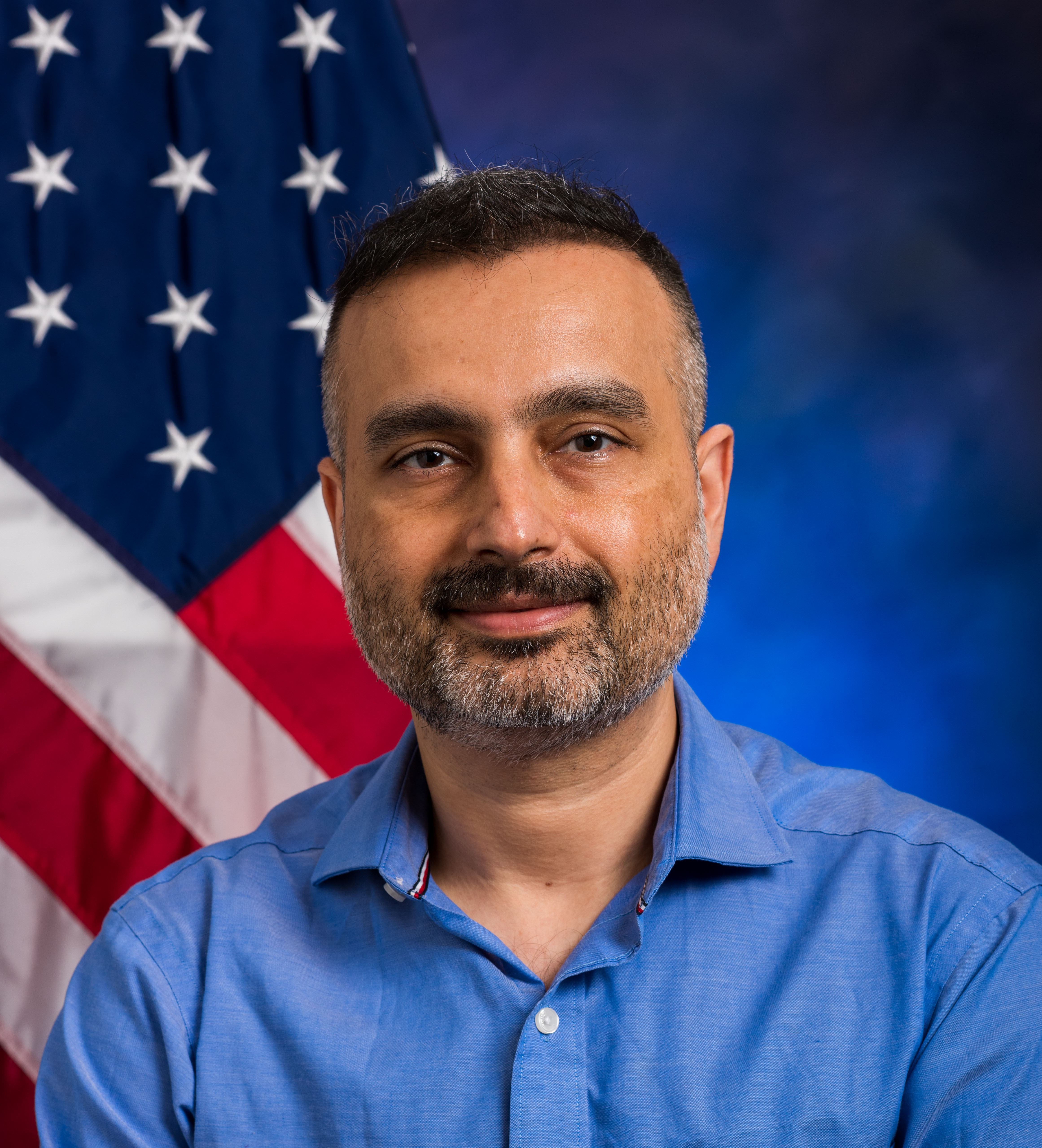 Headshot of Dr. Bajaj. He is smiling for the photo and wearing a collared shirt with an American flag behind him.