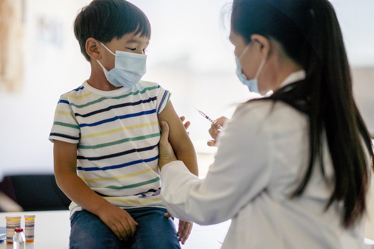 Young boy wearing a mask receiving a vaccine from woman wearing lab coat and mask