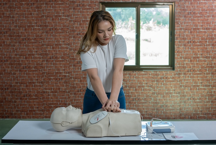 Woman stands with her hands over the heart area of a  CPR manikin.