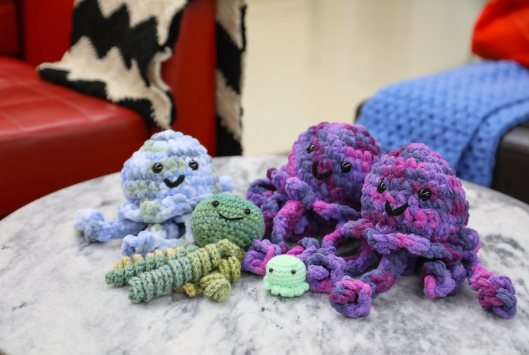 crocheted jellyfish stuffed animals in blue, purple and green are on top of a marble coffee table. The toys all have smiley faces on them.