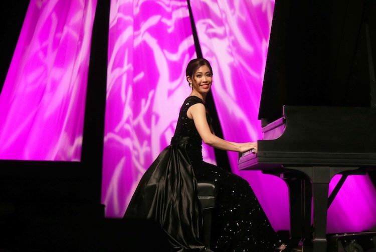 Woman playing piano and smiling while wearing a black ballgown