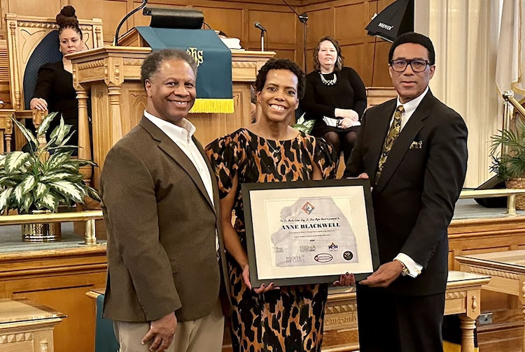 Three people stand together in a church receiving an award.