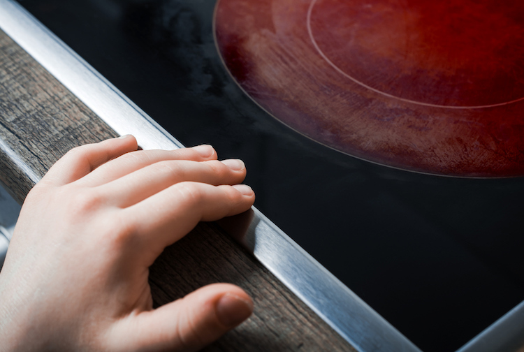 A child's hand reaches across an active hot stove top.