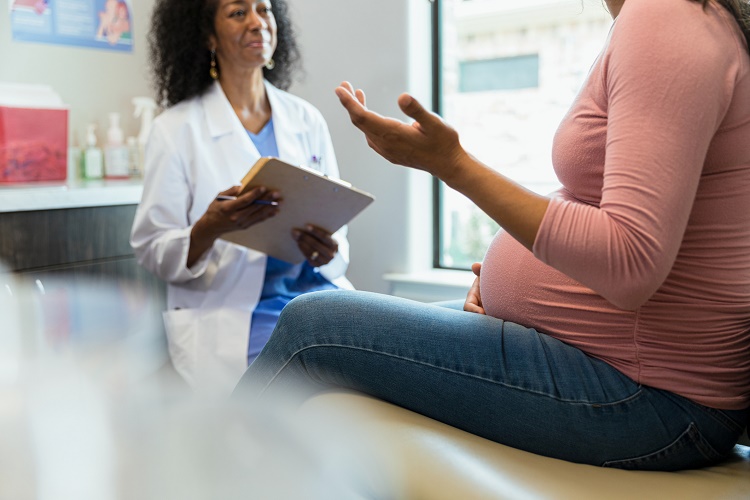 African-American female doctor sitting down and smiling at pregnant patient
