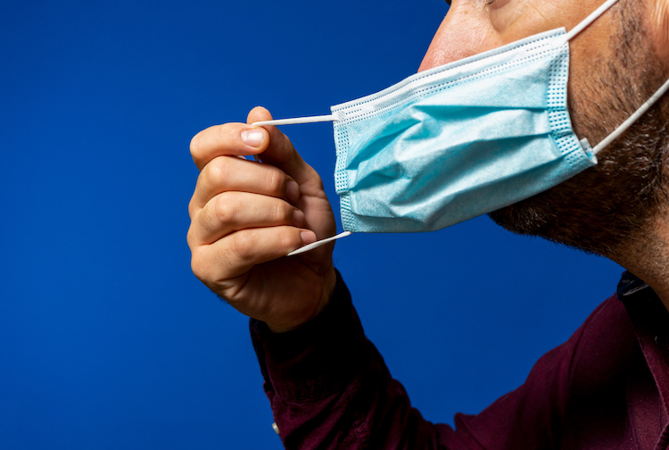 Man taking off his surgical mask isolated on blue background.