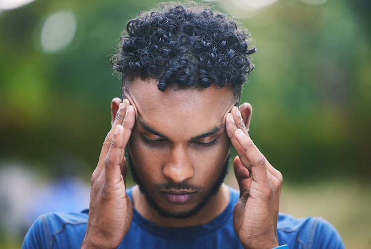 Man with headache in nature after workout. He is holding his head with a pained look on his face.