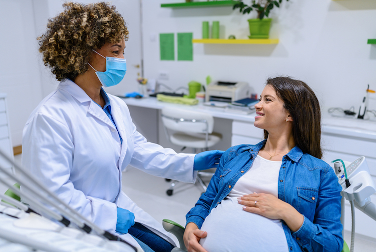 Pregnant patient sitting in a chair. She is smiling while talking to a doctor.