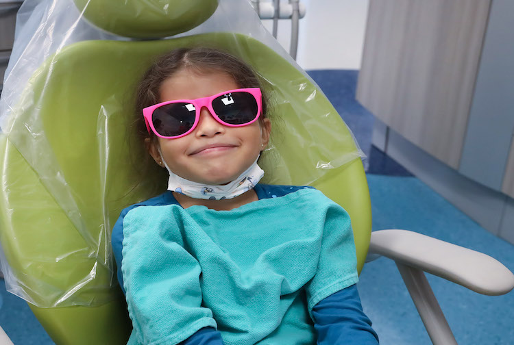 Young girl smiling in a dentist chair with sunglasses on.