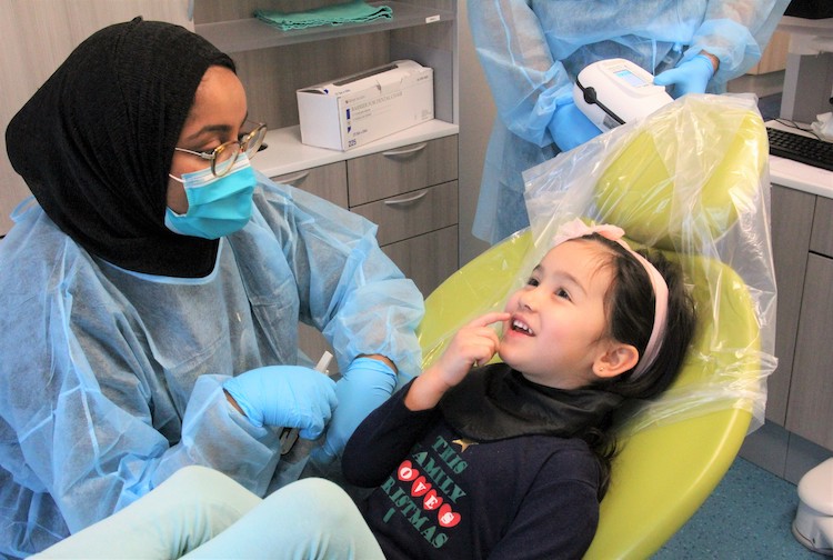 Child sits in a dentists' chair and talking with a dental student about her tooth.