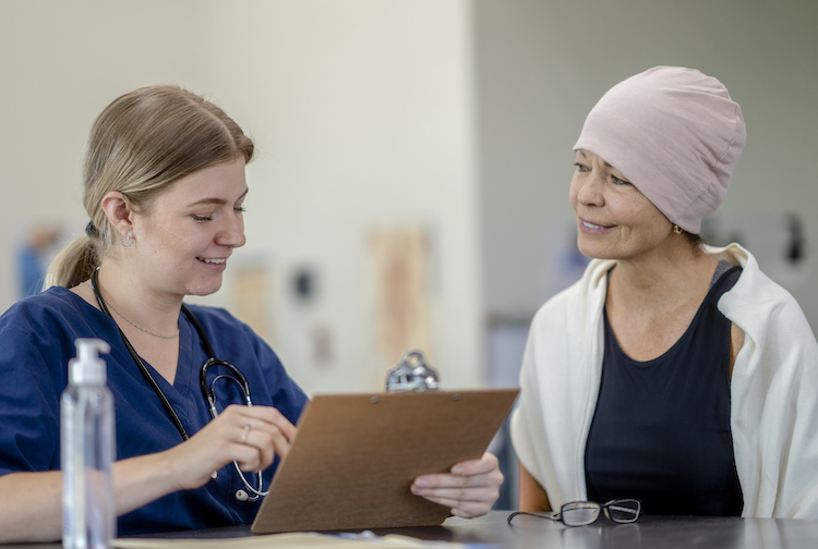 Woman provider with a clipboard speaking to a woman patient who has a pink hat on.