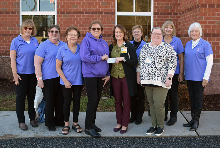 a group of ladies in purple polo shirts give a check to a cancer center director