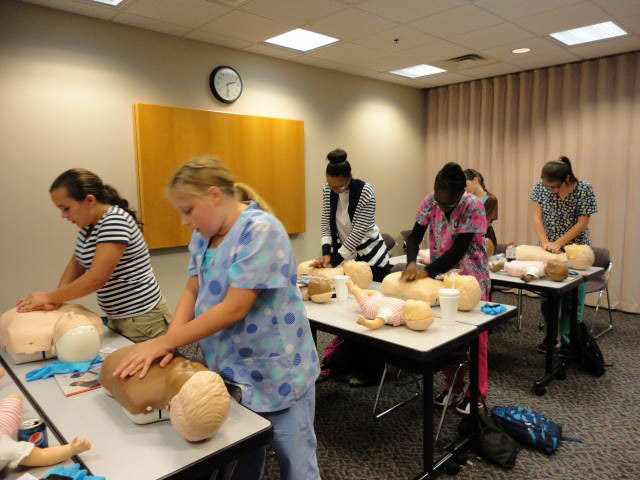 A group of teenagers learn CPR in a classroom.