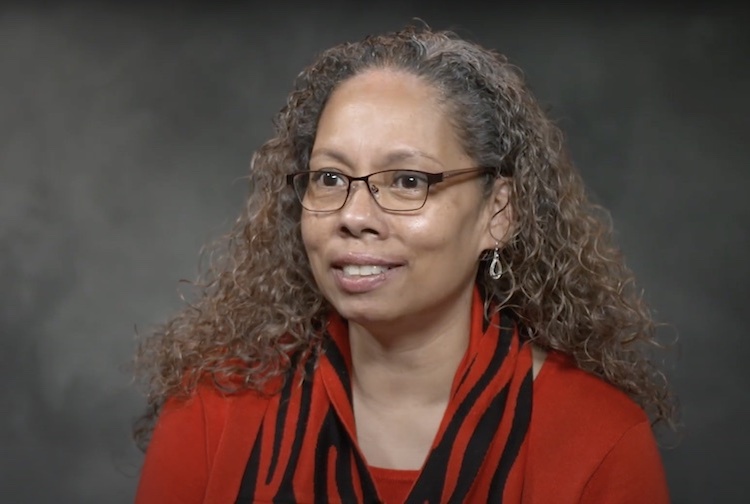 Portrait of Marcelle Davis from a video of her speaking about DEI initiatives. She is wearing a red shirt and glasses.