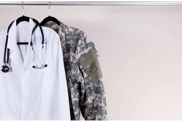 Clothes hanging on rack -- one is military-style jacket, the other a lab coat with stethoscope