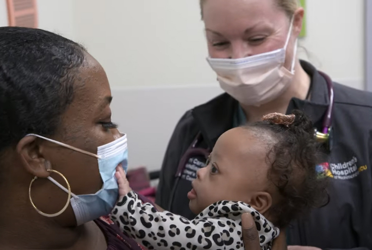 Mother and newborn baby smile at each other, while a Children's Hospital of Richmond at VCU team member is providing assistance.