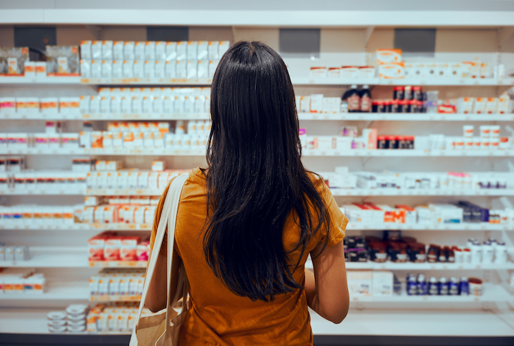 Young woman standing against shelf in pharmacy searching for medicine.