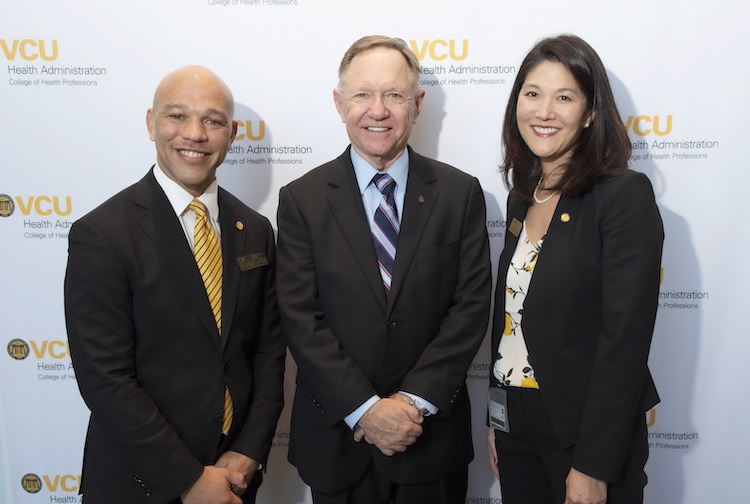 Three people standing in front of a white VCU College of Health professions background at an event.