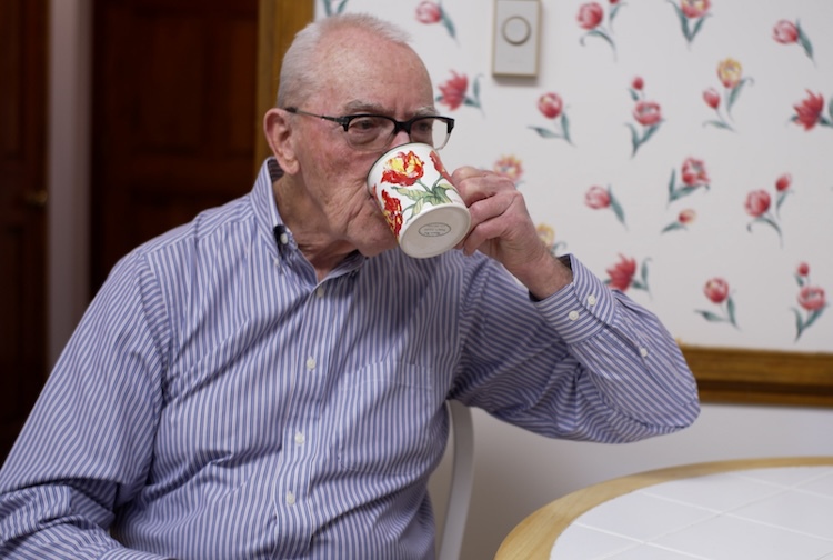 Older man sitting at a kitchen table and sipping coffee