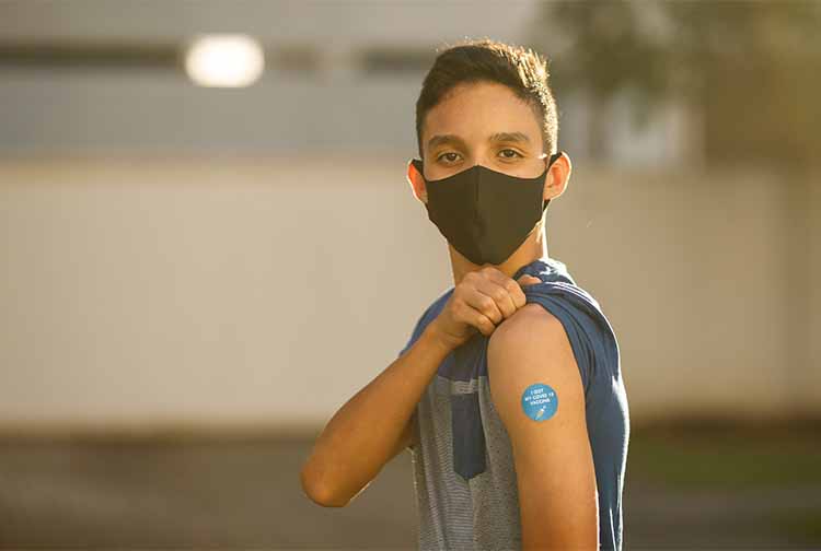 Teen wearing mask showing the spot on his arm where he got vaccinated