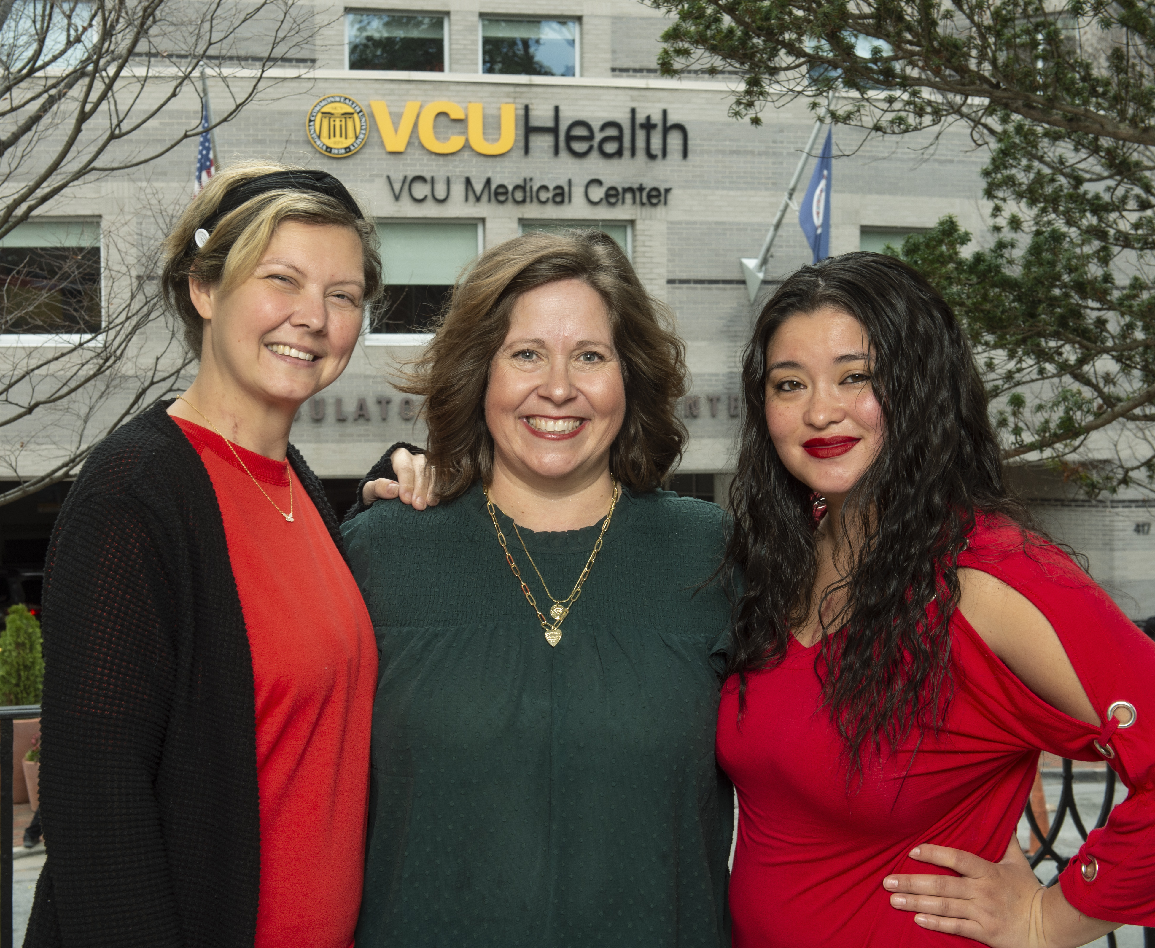 Three women standing together smiling. They are outside of a building at VCU Health.