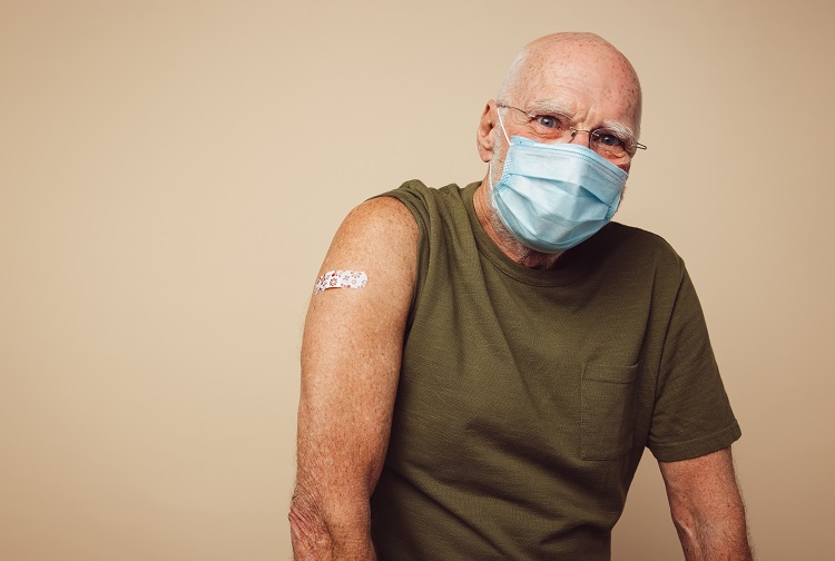 An older adult wears a mask and a bandage on his upper arm after receiving a COVID-19 vaccination.
